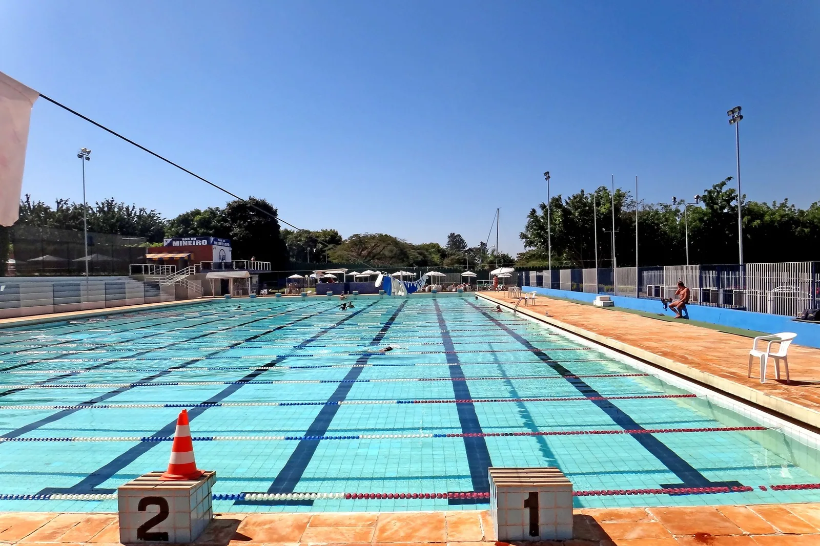 Piscina olímpica do clube AABB de Brasília, em dia de sol, com raias marcadas e cones nos blocos de partida.