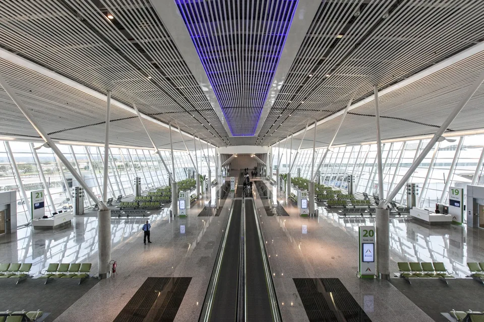 Salão de embarque do Aeroporto Internacional de Brasília, com esteiras rolantes no centro e portões numerados, em foto de arquivo