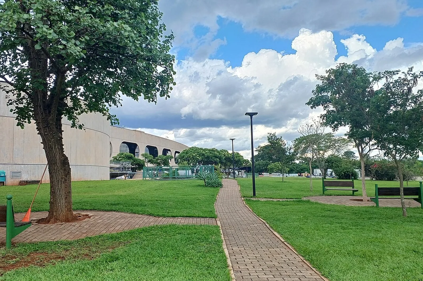 Jardim do CCBB Brasília, com caminho de tijolos, gramado e o prédio de concreto com janelas ovais ao fundo