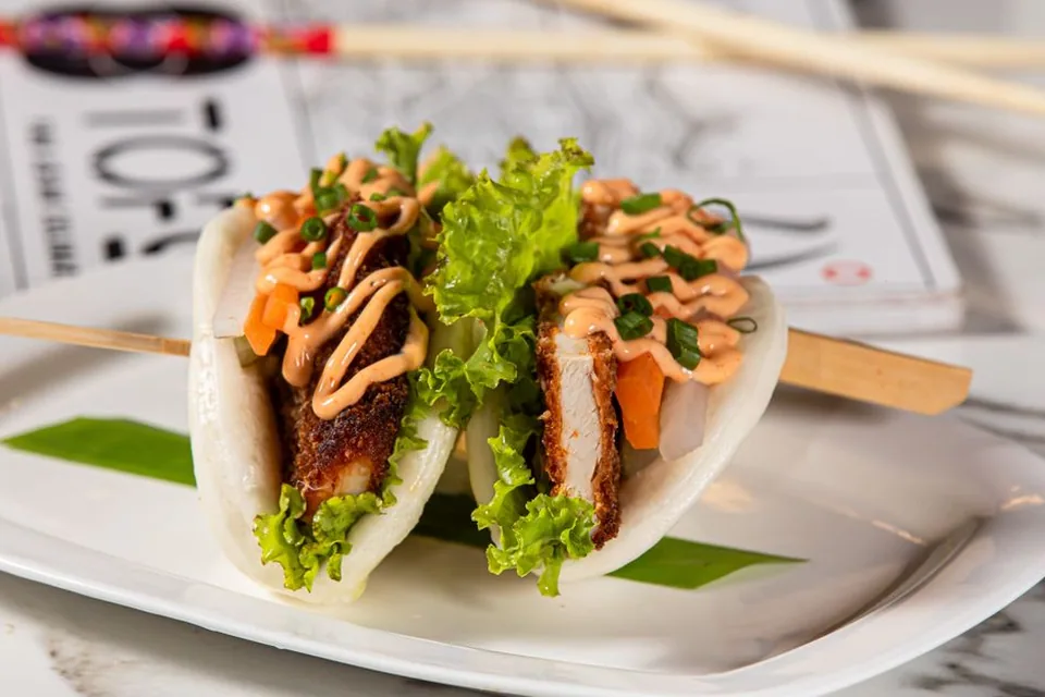 Dois pãezinhos bao recheados com frango empanado, alface e molho, em prato branco (foto ilustrativa, não é da casa)