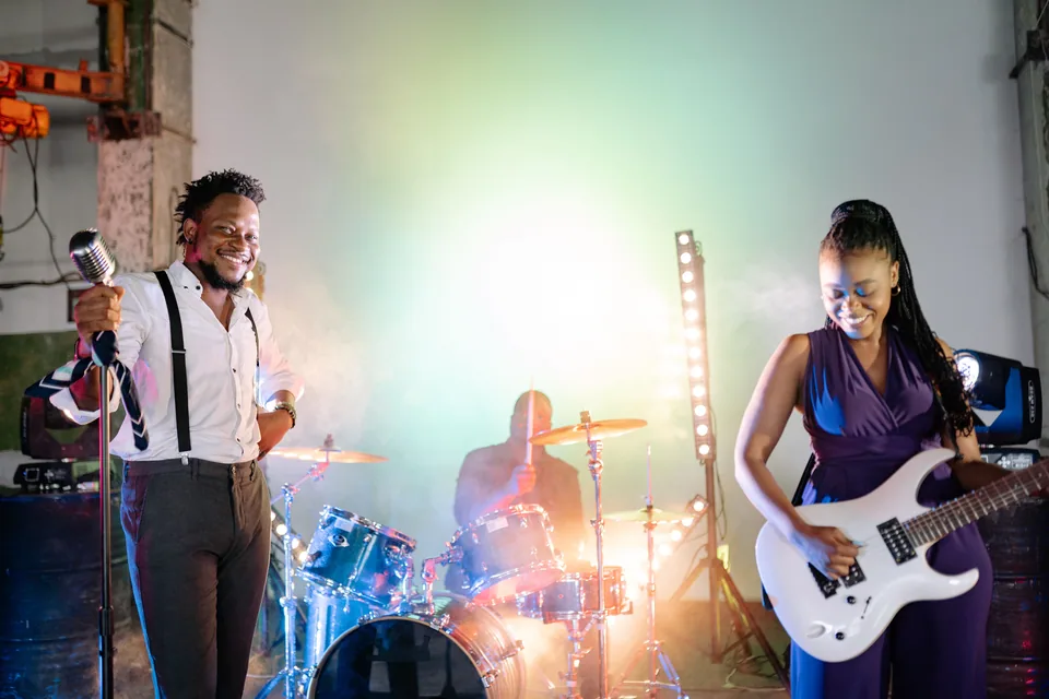 Banda tocando ao vivo em palco com fumaça e luzes: vocalista ao microfone, baterista ao fundo e guitarrista com guitarra branca