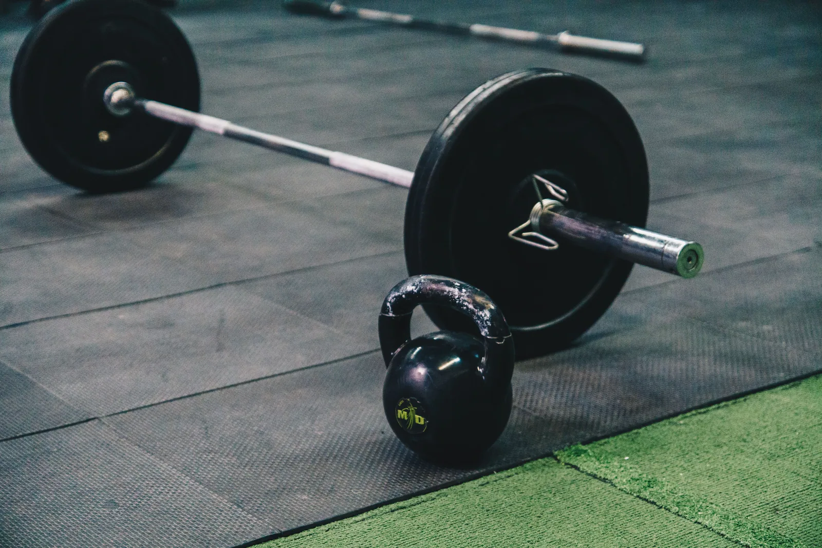 Barra com anilhas e kettlebell no piso emborrachado de uma academia