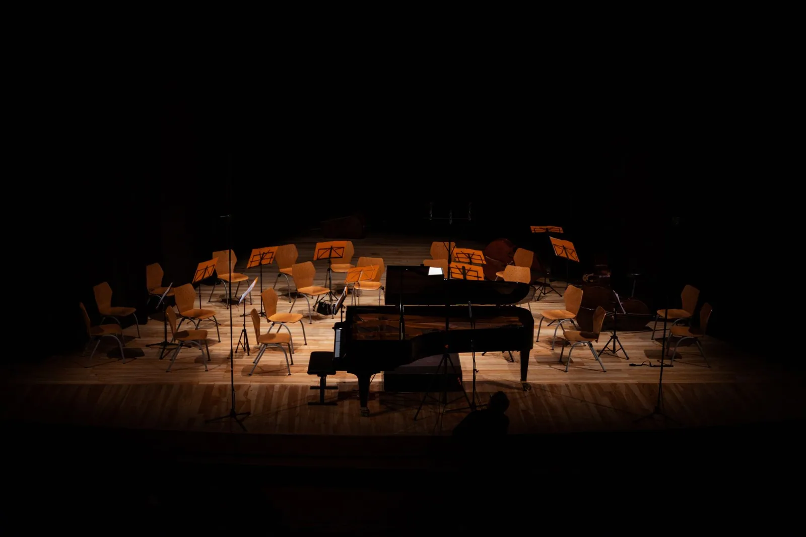 Palco de teatro com piano de cauda e cadeiras de orquestra sob luz de refletor