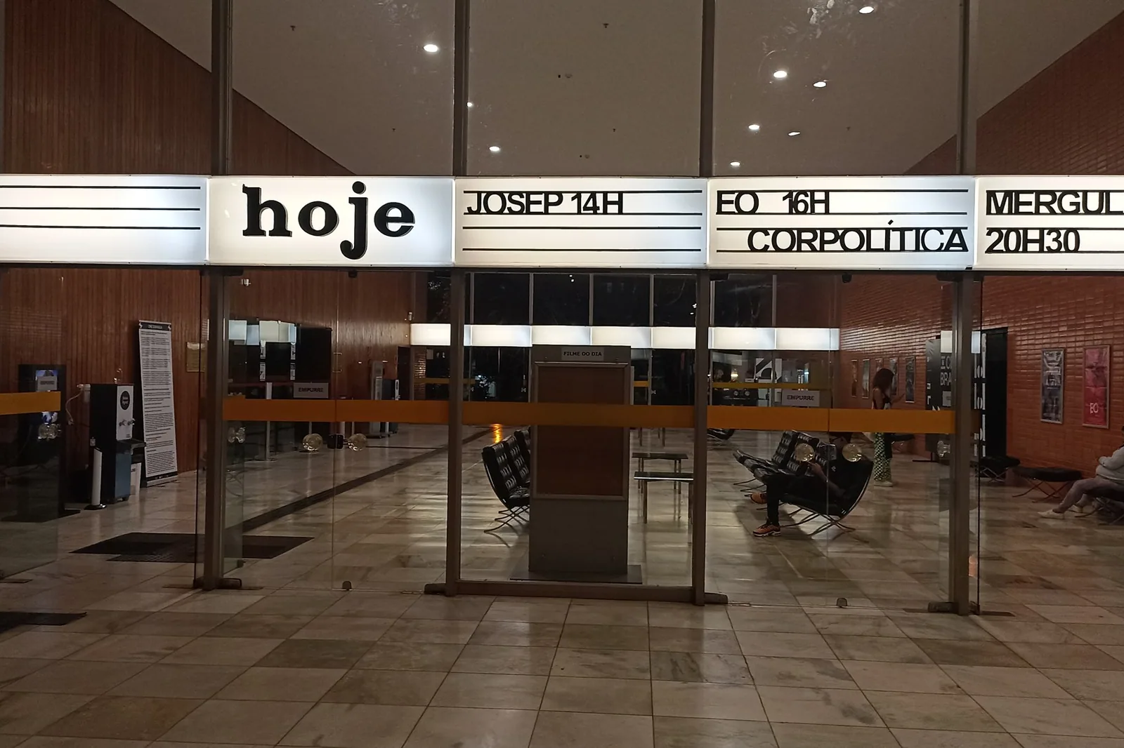 Saguão do Cine Brasília visto da calçada, com o letreiro iluminado de programação sobre a entrada
