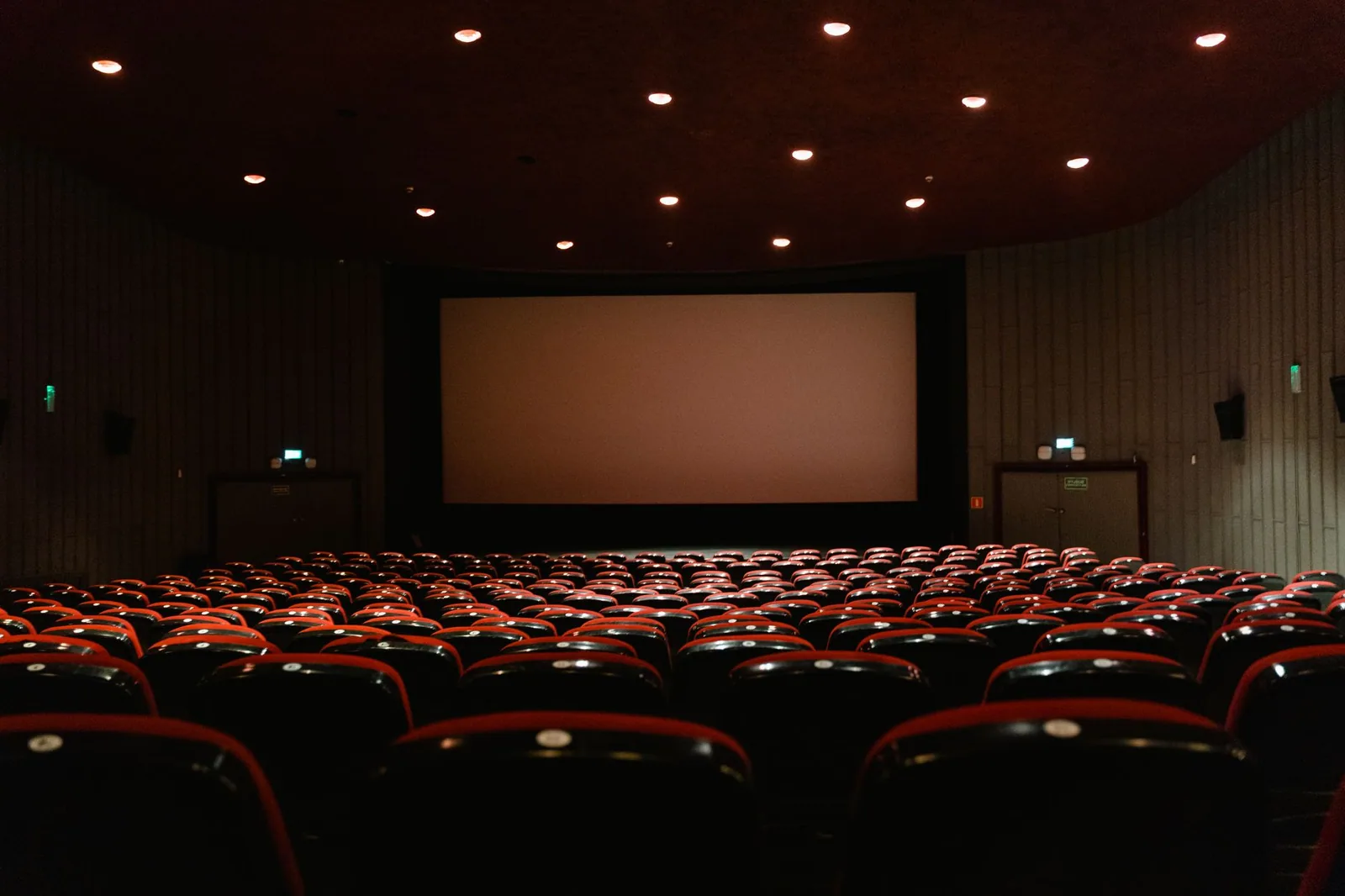 Sala de cinema com fileiras de poltronas vermelhas voltadas para a tela