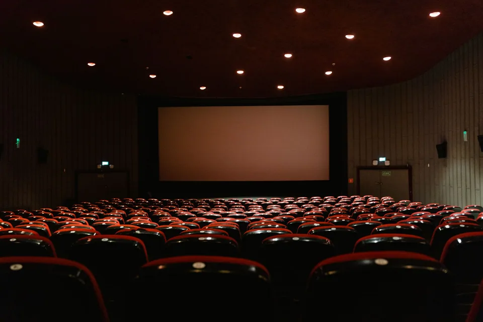 Sala de cinema com fileiras de poltronas vermelhas voltadas para a tela