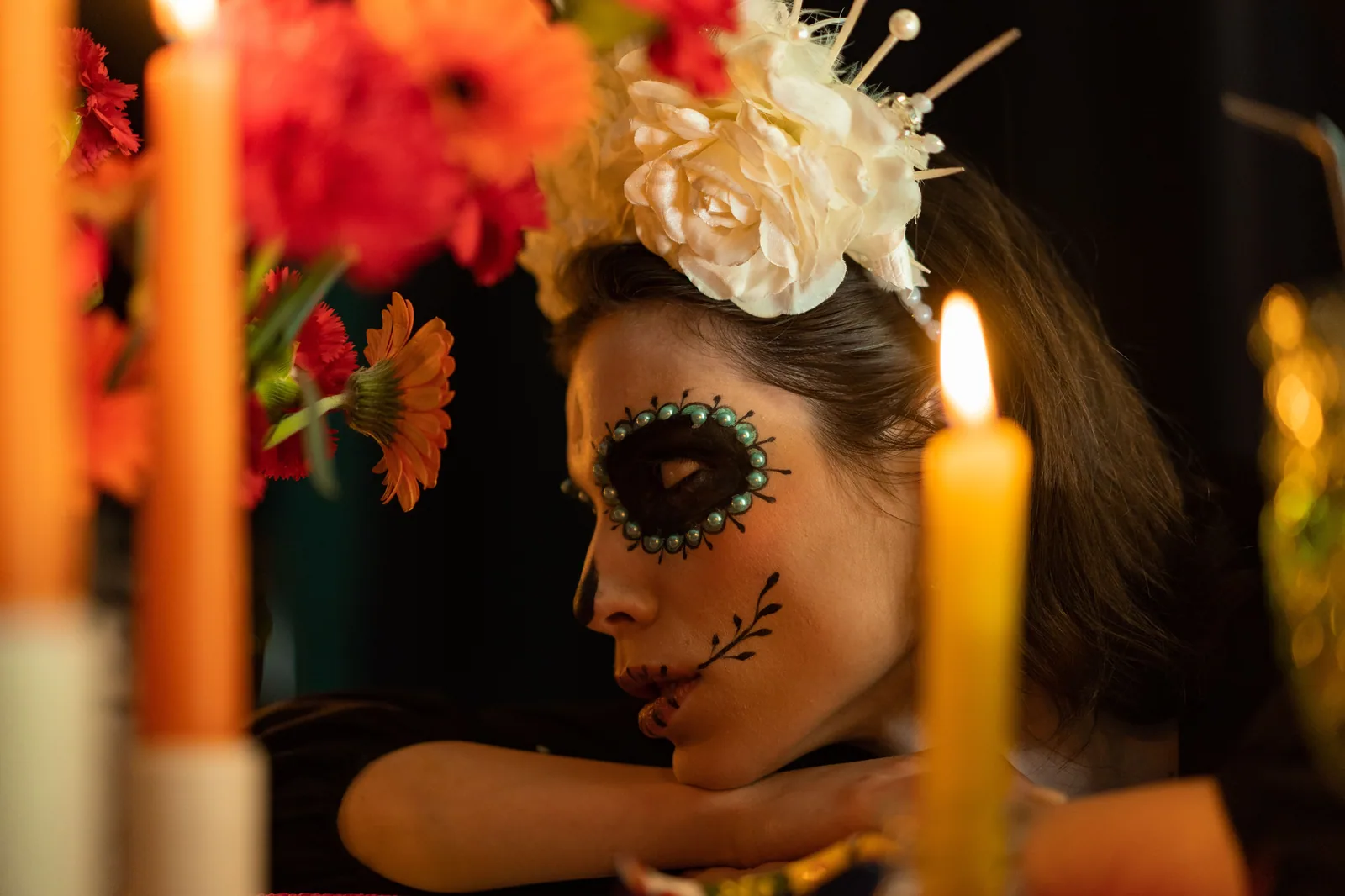 Mulher com maquiagem de caveira mexicana, flores na cabeça e velas acesas, em foto ilustrativa