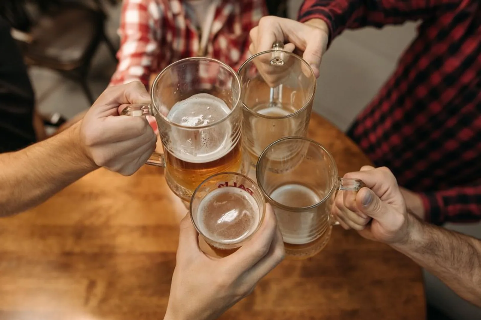 Mãos brindando com canecas de chope sobre mesa de madeira