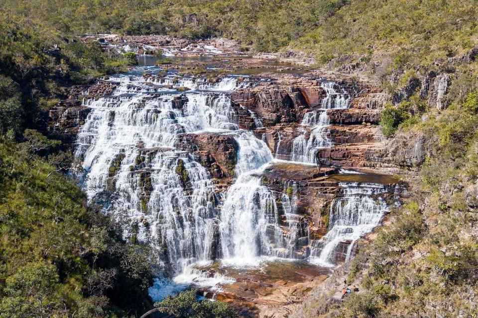 Cachoeira em degraus de rocha avermelhada cercada por vegetação de cerrado (foto ilustrativa)