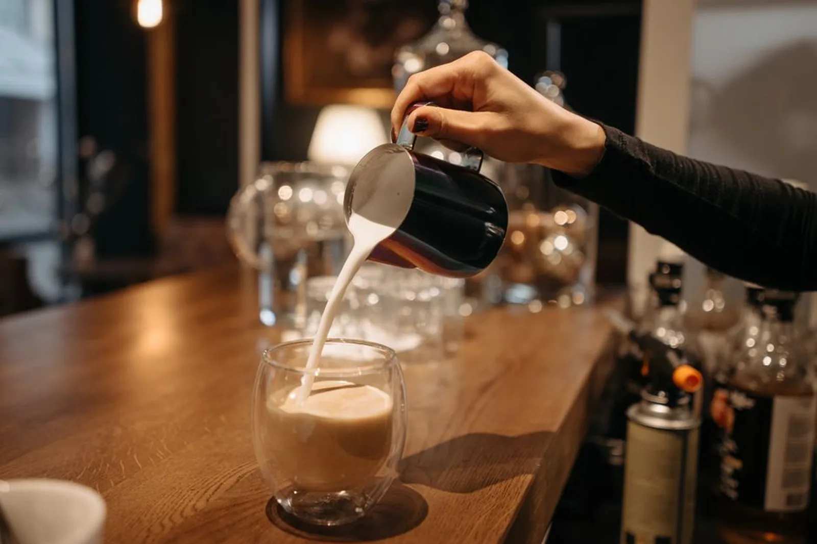 Barista despejando leite vaporizado em um copo de café sobre balcão de madeira