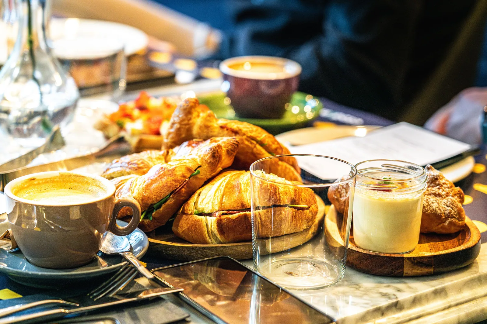 Mesa de café com croissants, xícara de café com leite e potes de creme, vista de perto