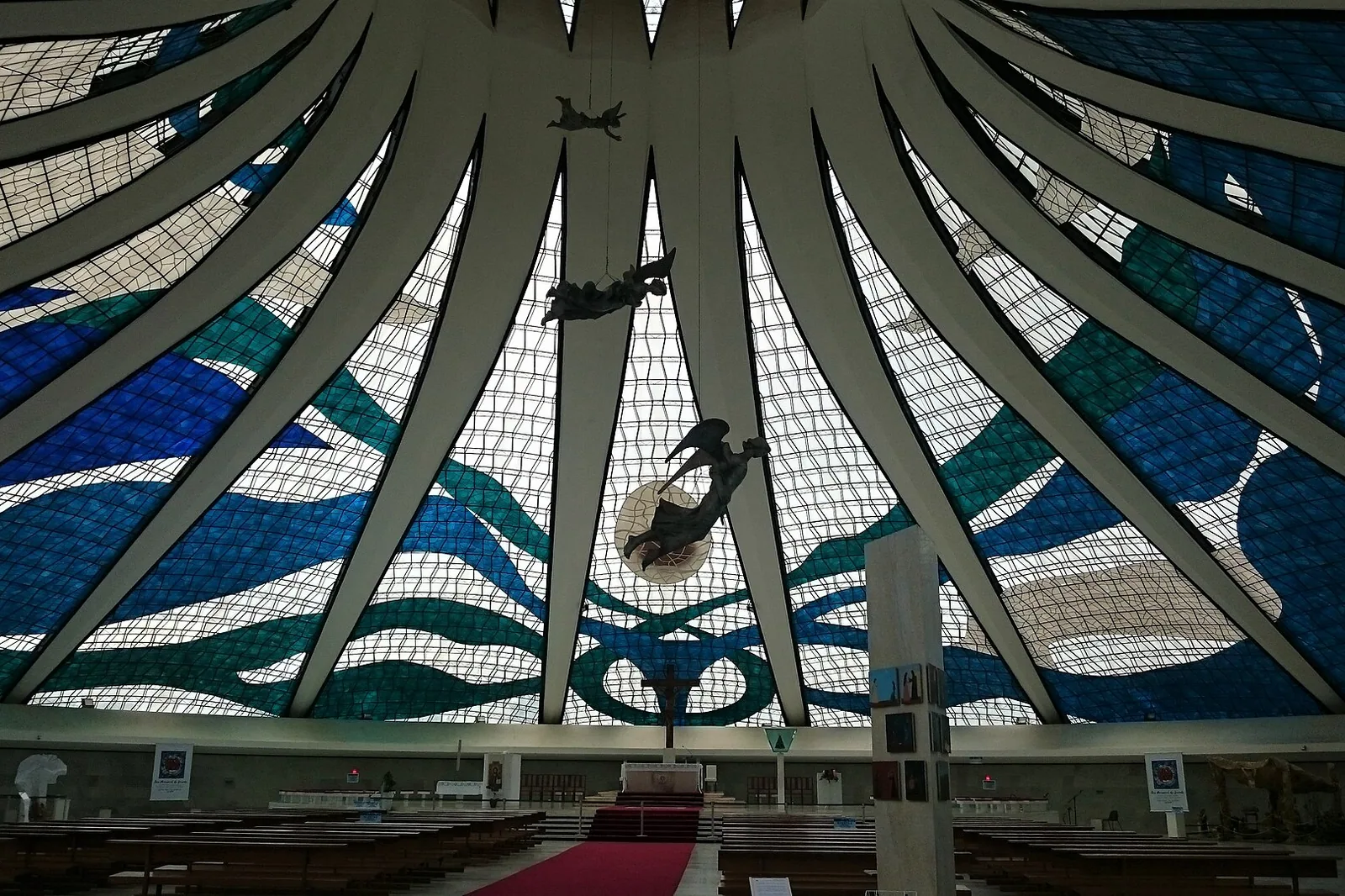 Interior da Catedral de Brasília visto da entrada, com os vitrais azuis e verdes, os anjos suspensos e o altar ao fundo