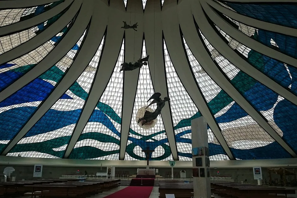 Interior da Catedral de Brasília visto da entrada, com os vitrais azuis e verdes, os anjos suspensos e o altar ao fundo