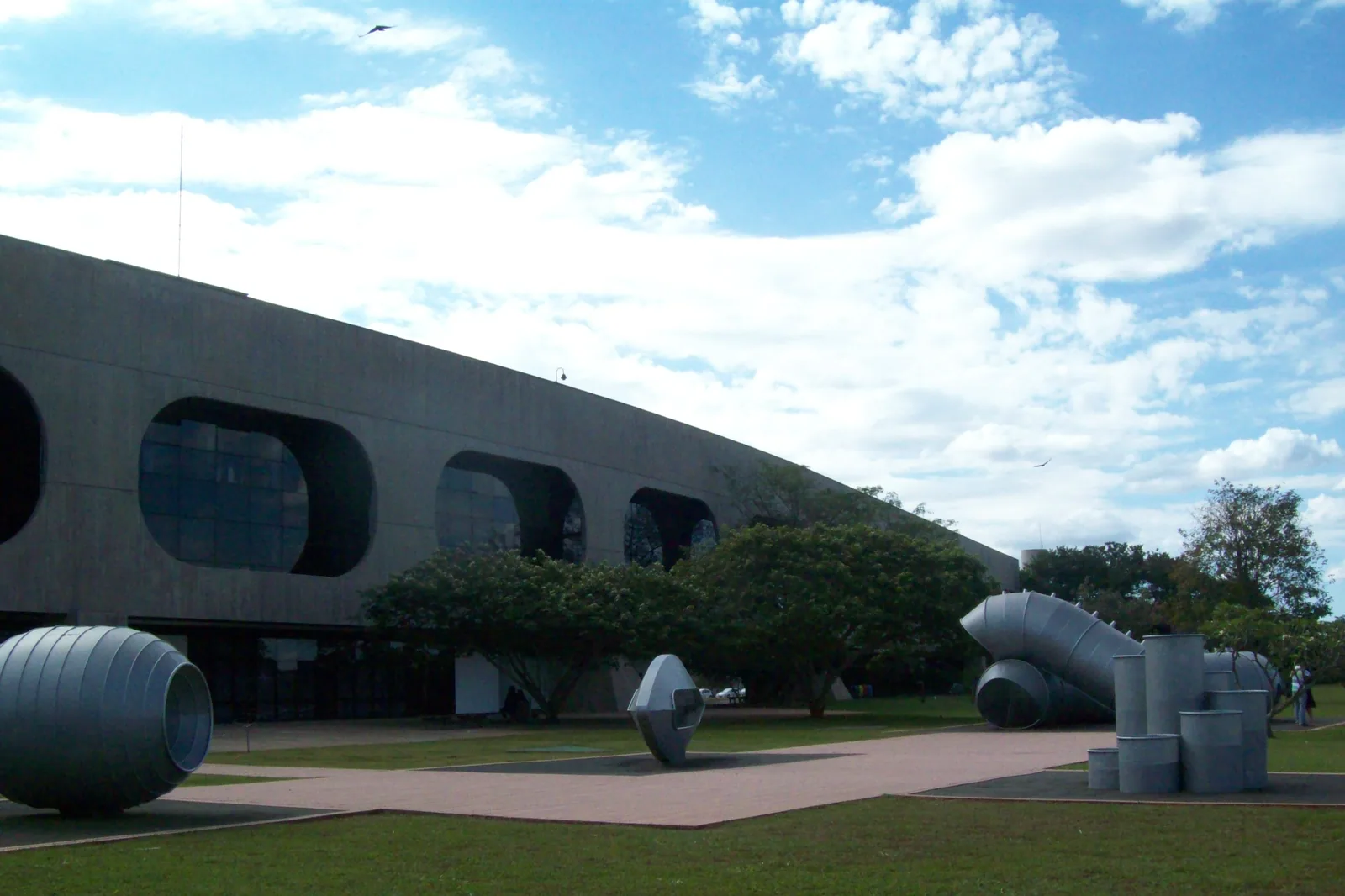 Esculturas metálicas no gramado em frente ao prédio de concreto do CCBB Brasília, perto do Casulo