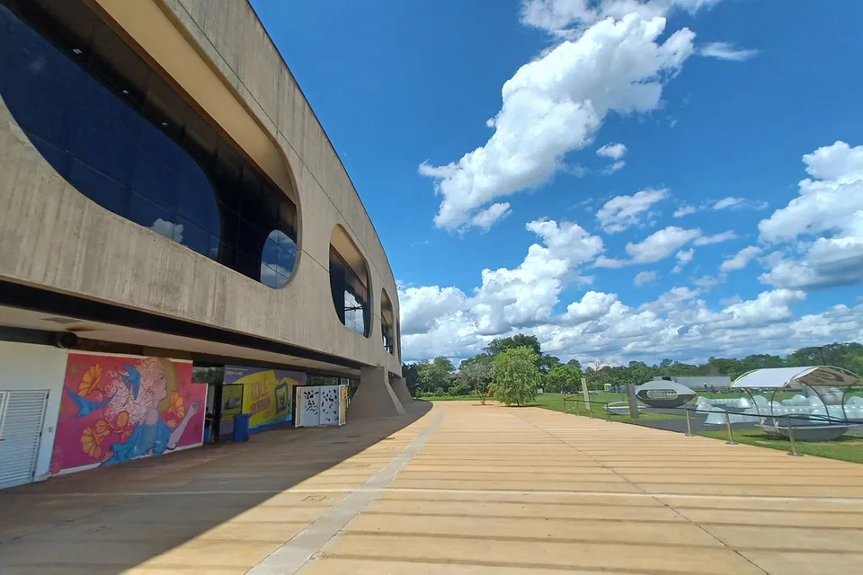 Fachada curva de concreto do CCBB Brasília, com janelas ovais e mural colorido, sob céu azul
