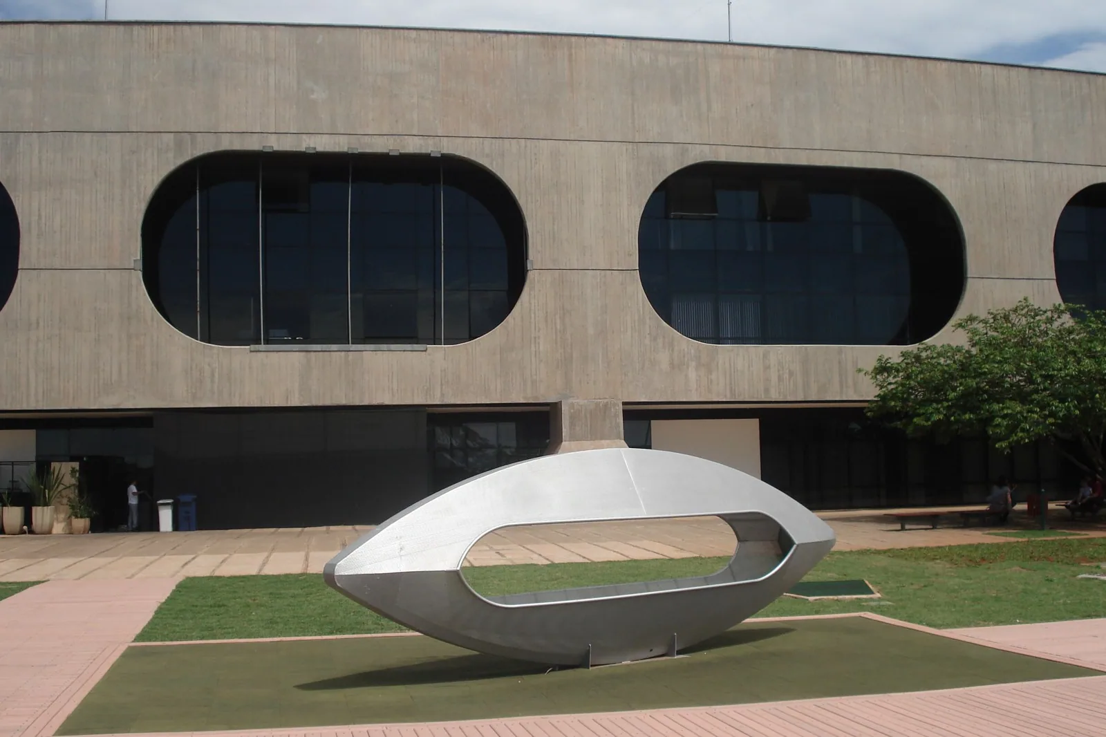 Escultura de aço em forma de casulo diante da fachada de concreto com janelas ovais do CCBB Brasília, em foto de arquivo