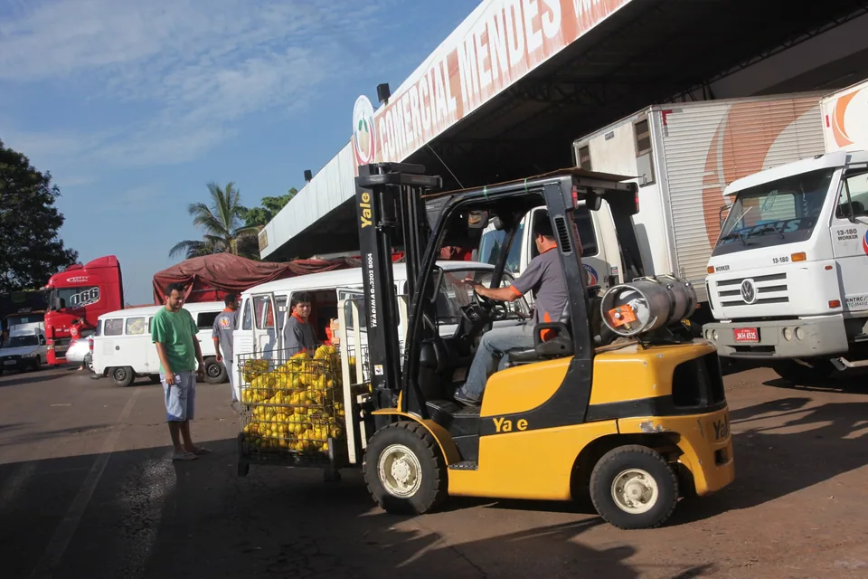 Empilhadeira carrega caixas de fruta numa doca da Ceasa-DF, com caminhões ao fundo, em foto de arquivo