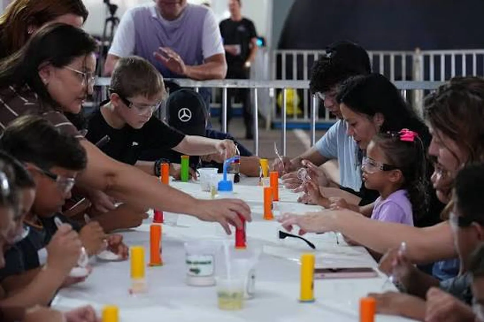 Crianças e adultos em volta de uma mesa fazendo experimento com tubos coloridos em oficina do Ciência na Estrada