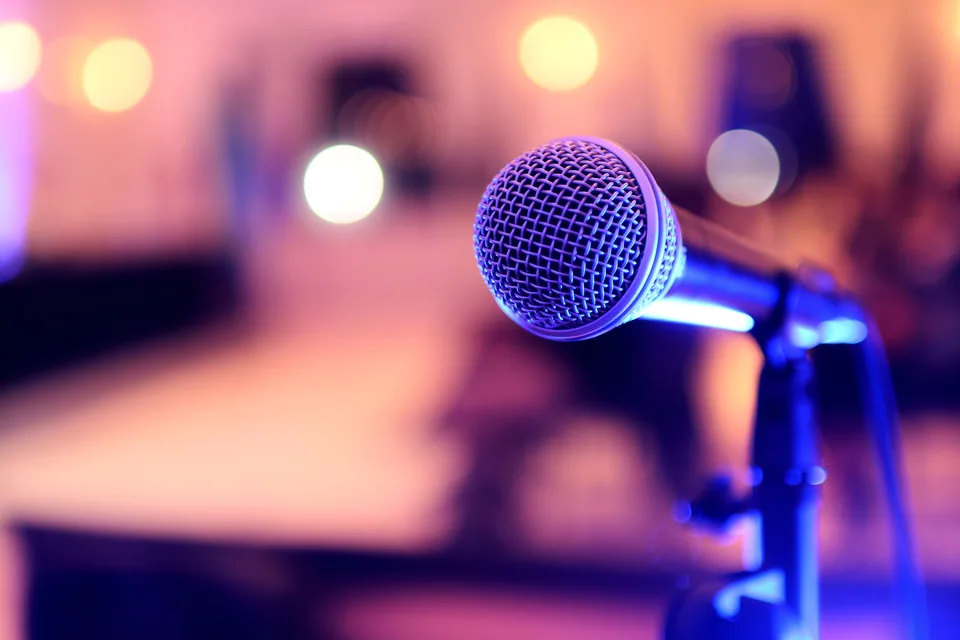 Microfone em pedestal no palco, com luzes coloridas desfocadas ao fundo