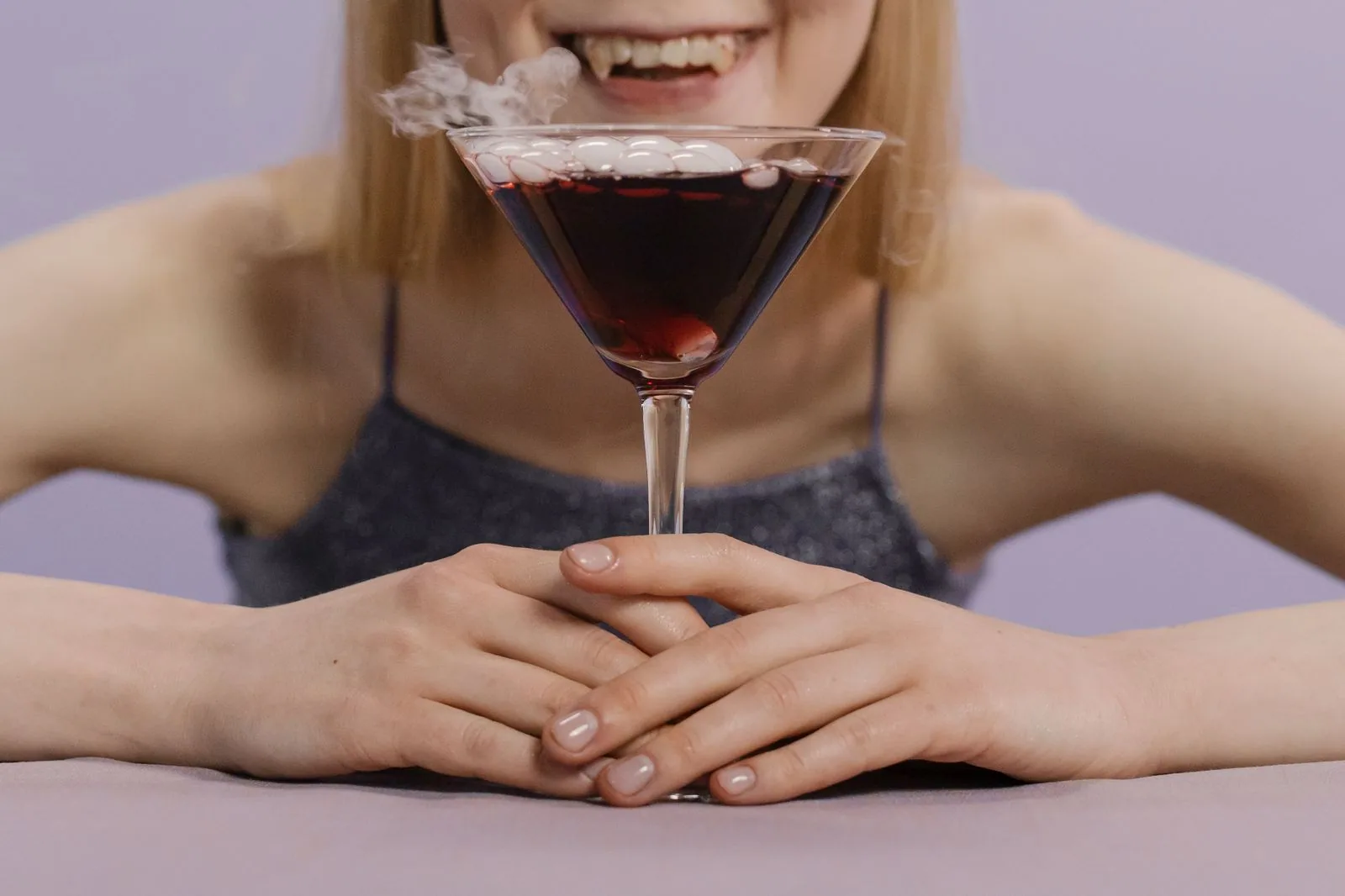 Mulher de presas de vampiro com uma taça de drink escuro e fumaça, foto de banco de imagens sem relação com o bar