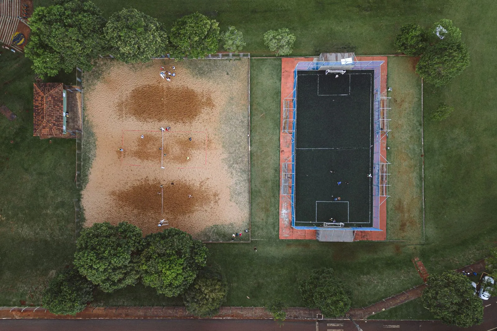 Vista aérea de quadras de areia e de uma quadra de society cercadas de árvores, com pessoas jogando