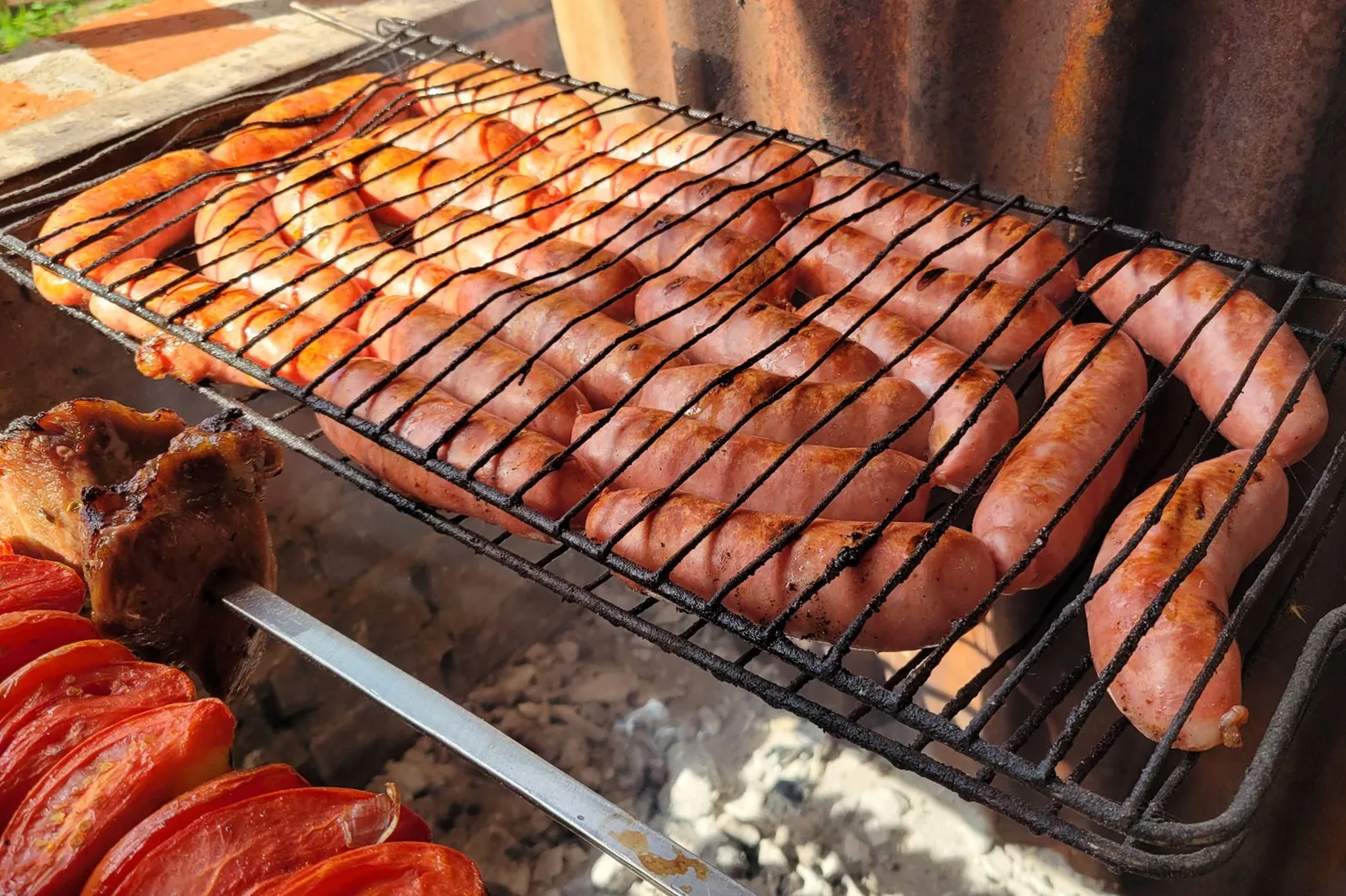 Linguiças assando sobre grelha de parrilla com brasa, foto ilustrativa de arquivo