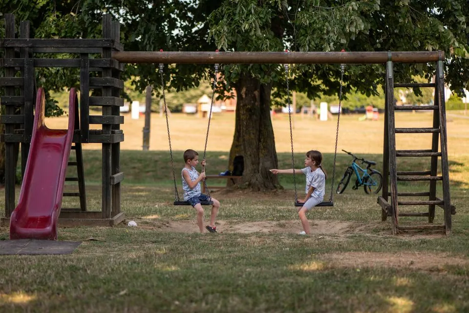 Crianças brincando em balanços em parque arborizado