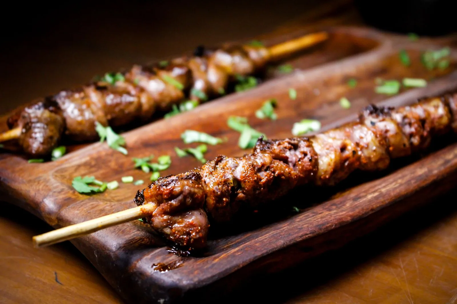 Espetinhos de carne grelhada servidos em tábua de madeira com cheiro-verde, foto ilustrativa de petisco de bar