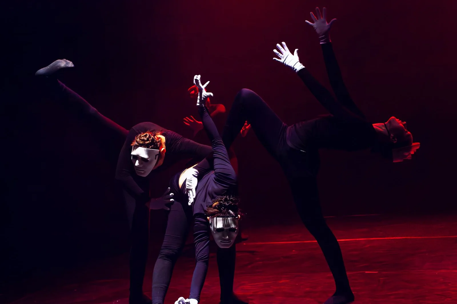 Três performers com máscaras brancas em palco com luz vermelha (foto ilustrativa, não é do espetáculo)