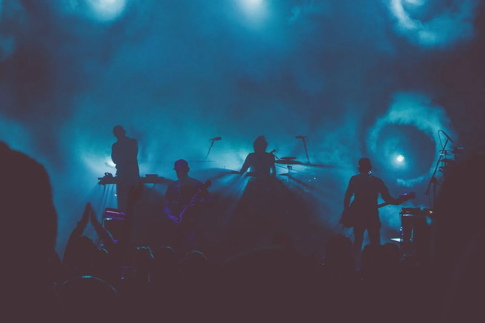 Banda em silhueta no palco, com luz azul e fumaça; foto ilustrativa, não é do show