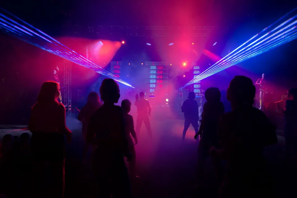 Pista de dança no escuro com lasers azuis e luz rosa e silhuetas de pessoas dançando