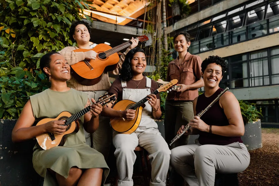 Cinco musicistas do Regional Severinas sorriem com cavaquinho, violão, bandolim e flauta nas mãos, em área externa com vegetação