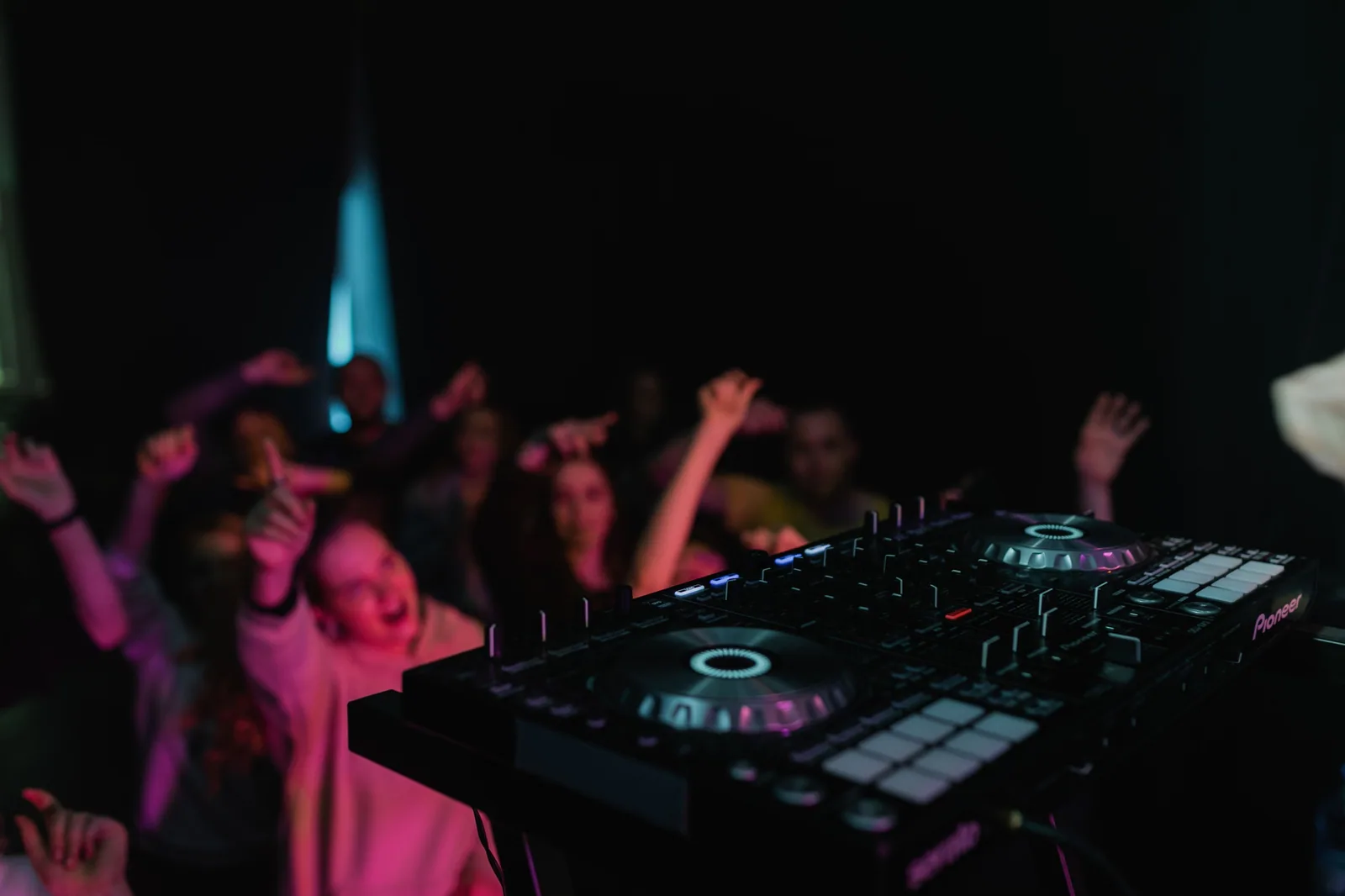 Controladora de DJ em primeiro plano e pessoas dançando ao fundo em uma pista escura