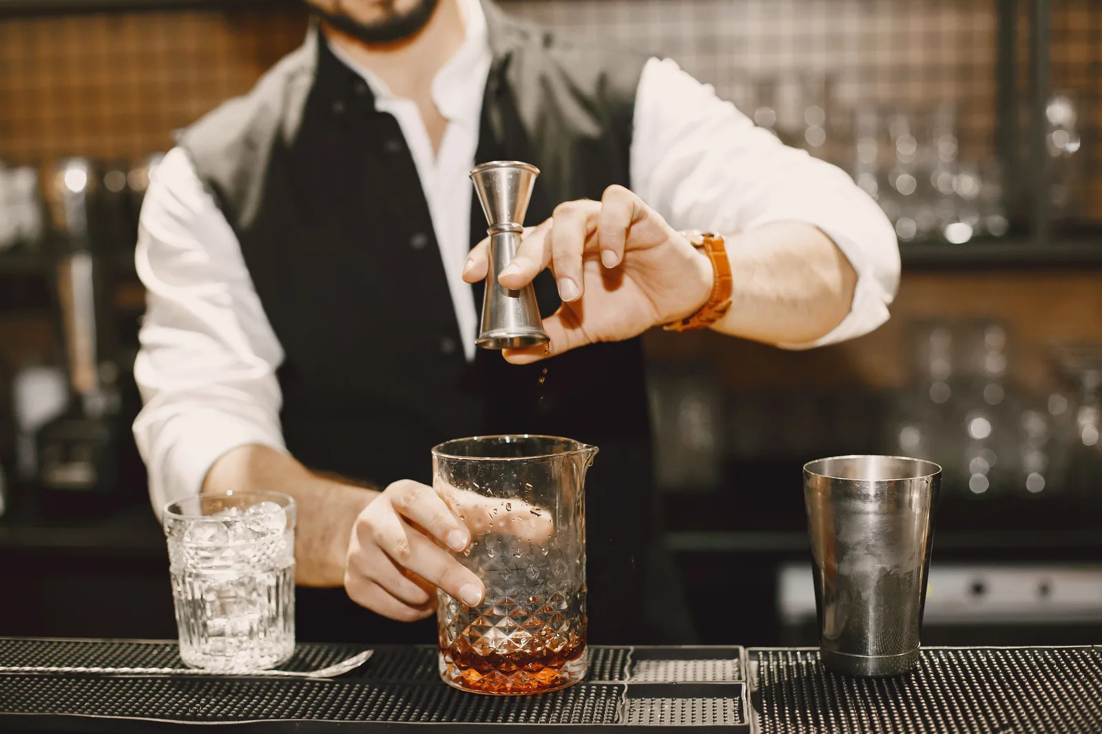 Bartender mede destilado com dosador sobre copo misturador no balcão do bar