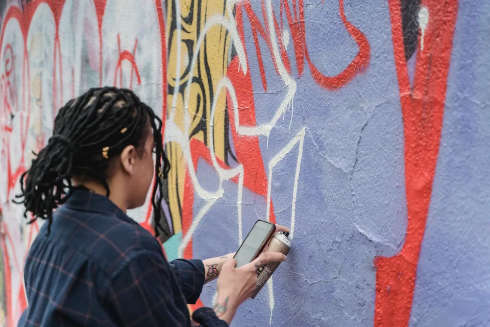 Artista de dreadlocks pinta com spray um muro coberto de grafite colorido