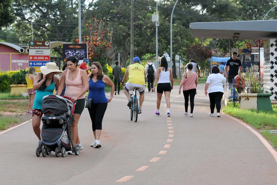 Pessoas caminham, correm e pedalam na pista do Parque da Cidade, em Brasília, ao lado de uma placa de percursos