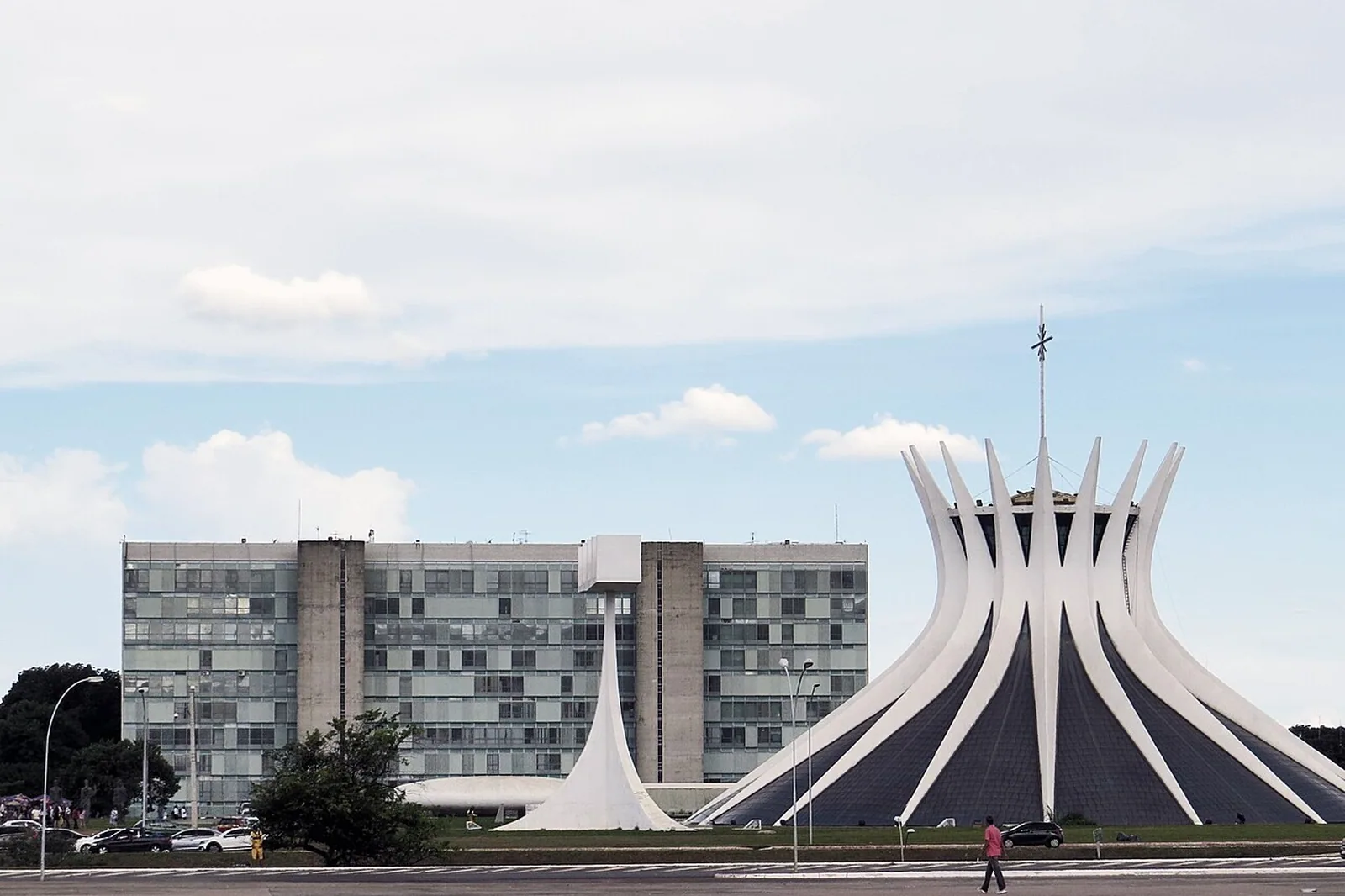 Catedral de Brasília e prédio dos ministérios vistos da Esplanada, com céu de nuvens claras