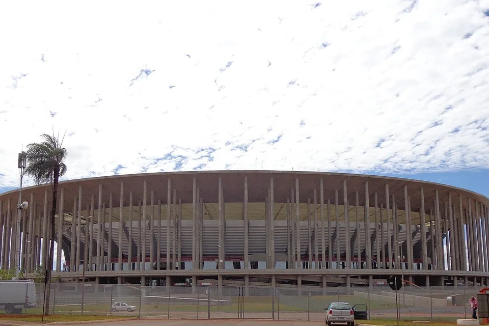 Fachada circular de concreto do Estádio Nacional Mané Garrincha, em Brasília, sob céu com nuvens finas