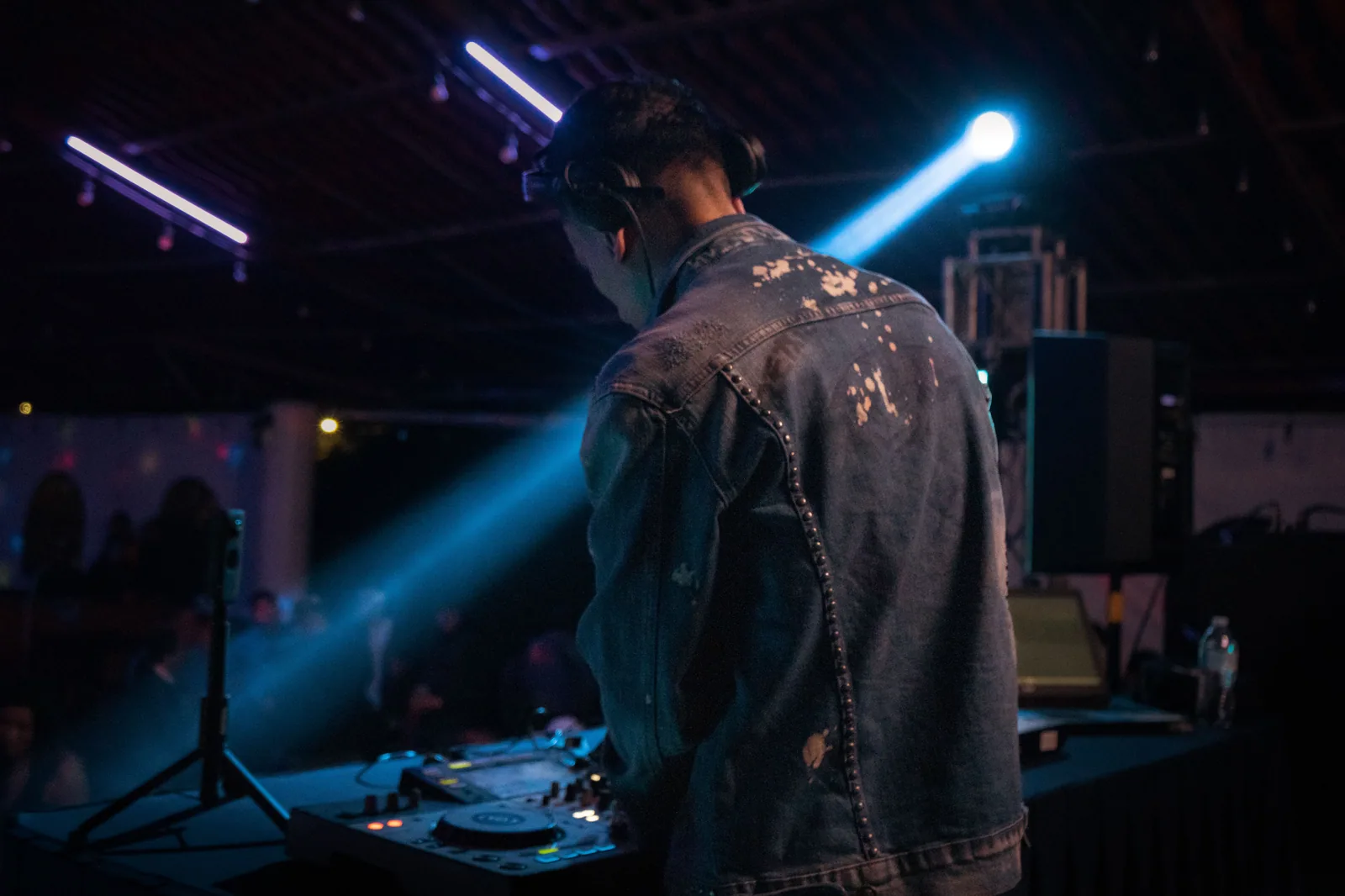 DJ de costas na mesa de som, com refletor azul ao fundo, em casa de show (foto ilustrativa)