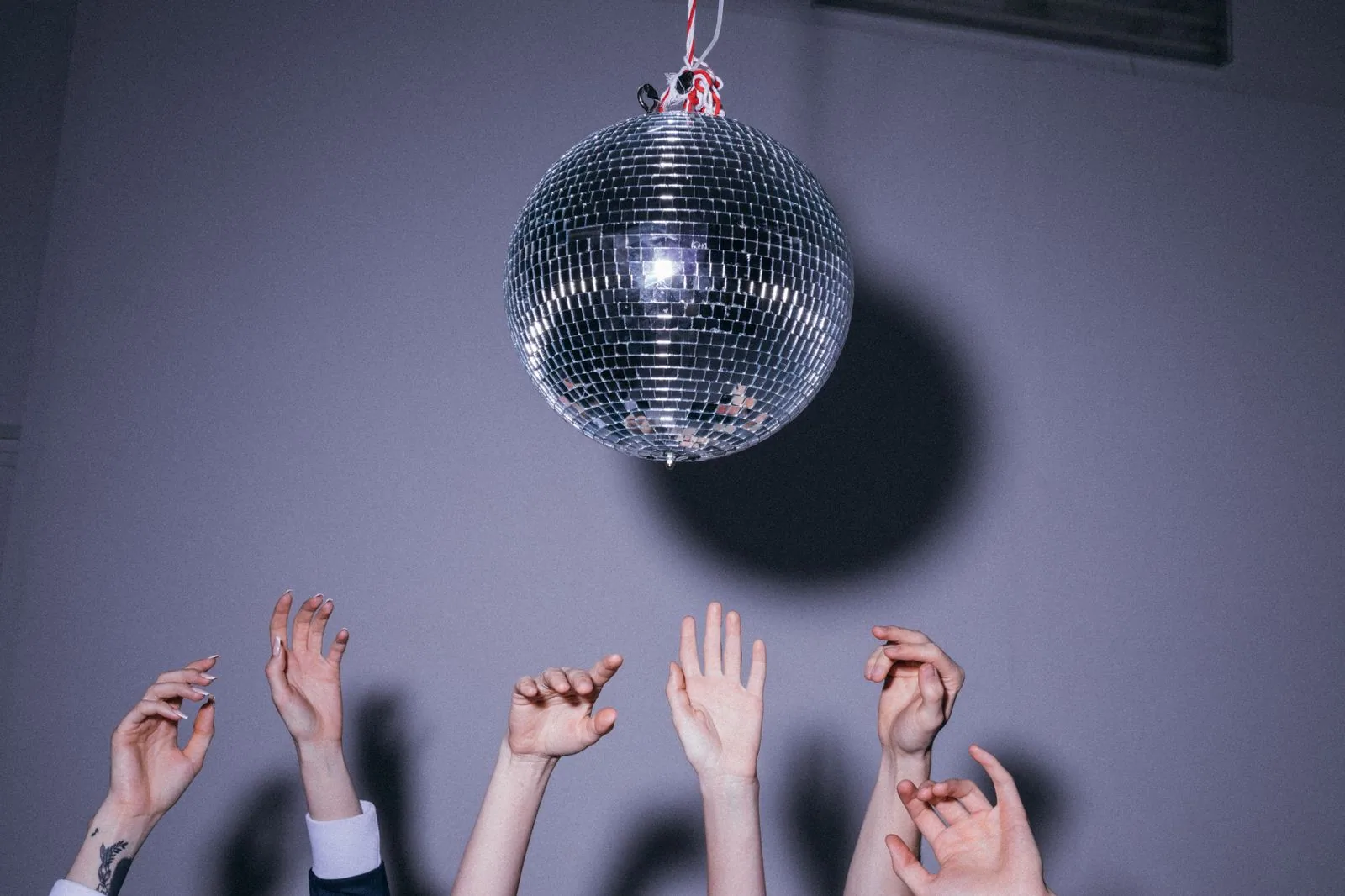 Mãos erguidas em direção a uma bola de espelhos, imagem ilustrativa de festa dance