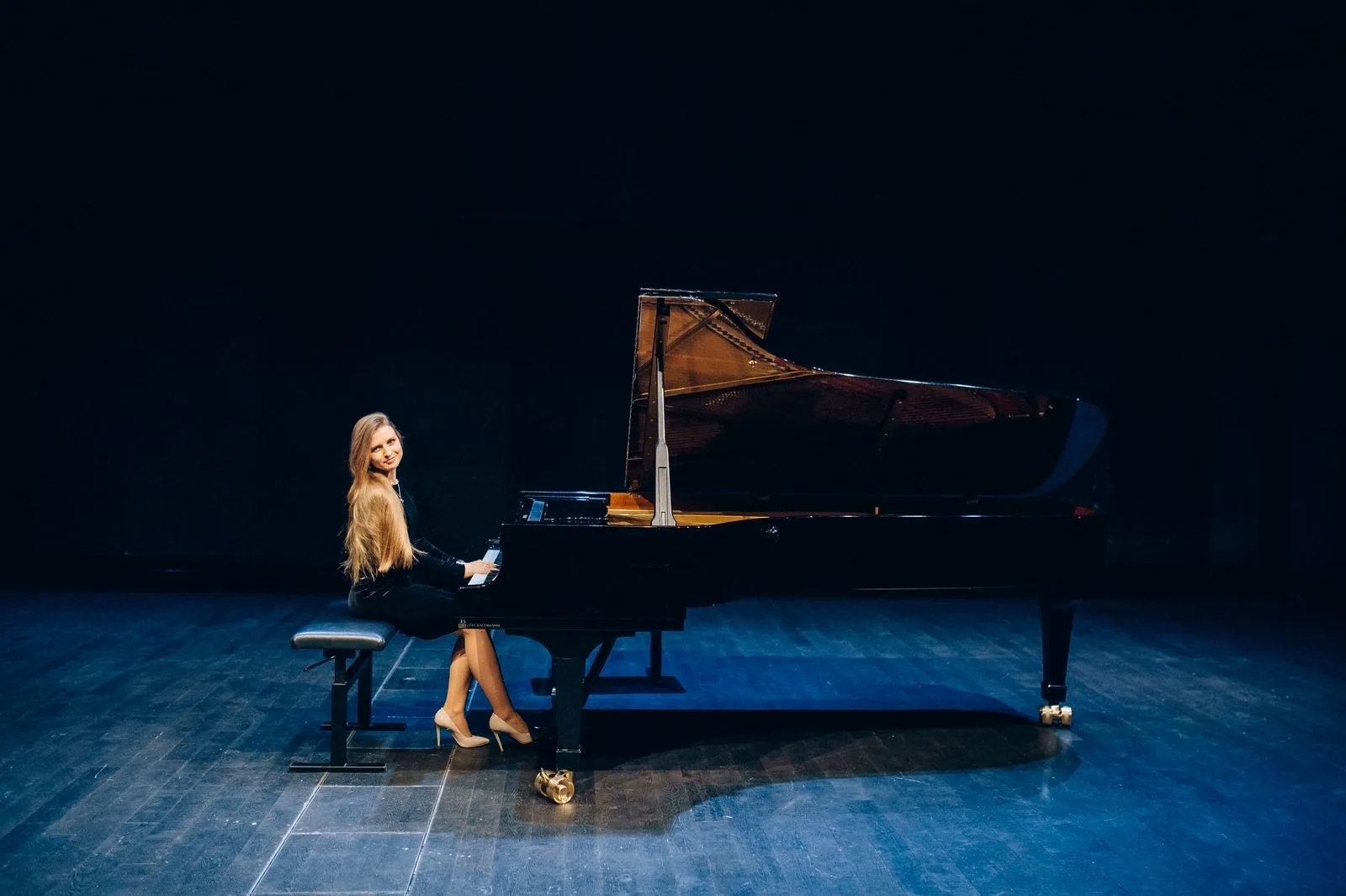 Pianista ao piano de cauda em palco escuro com luz azul, imagem ilustrativa