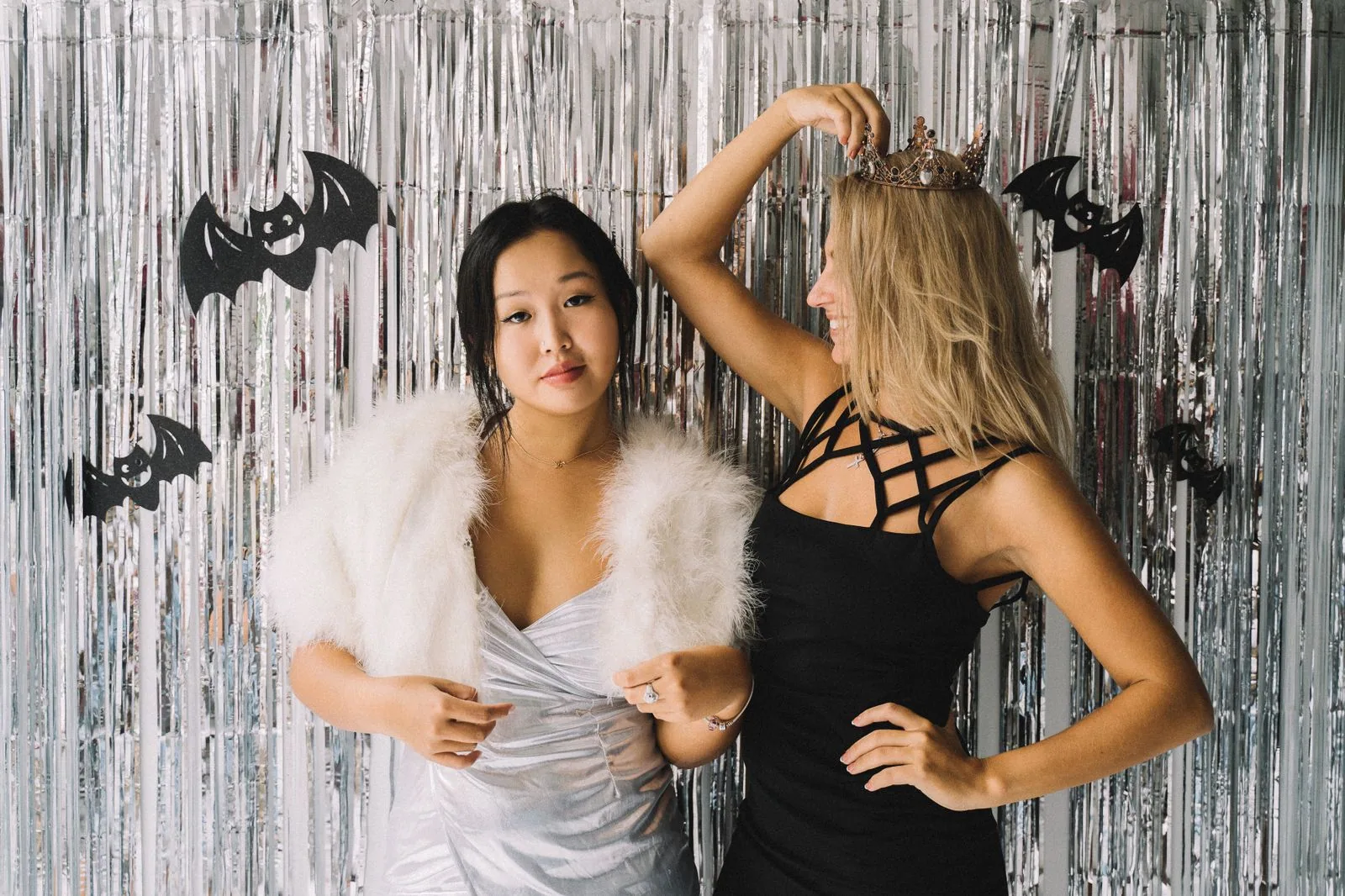 Duas mulheres posam com fantasia diante de uma cortina prateada com morcegos de papel de Halloween