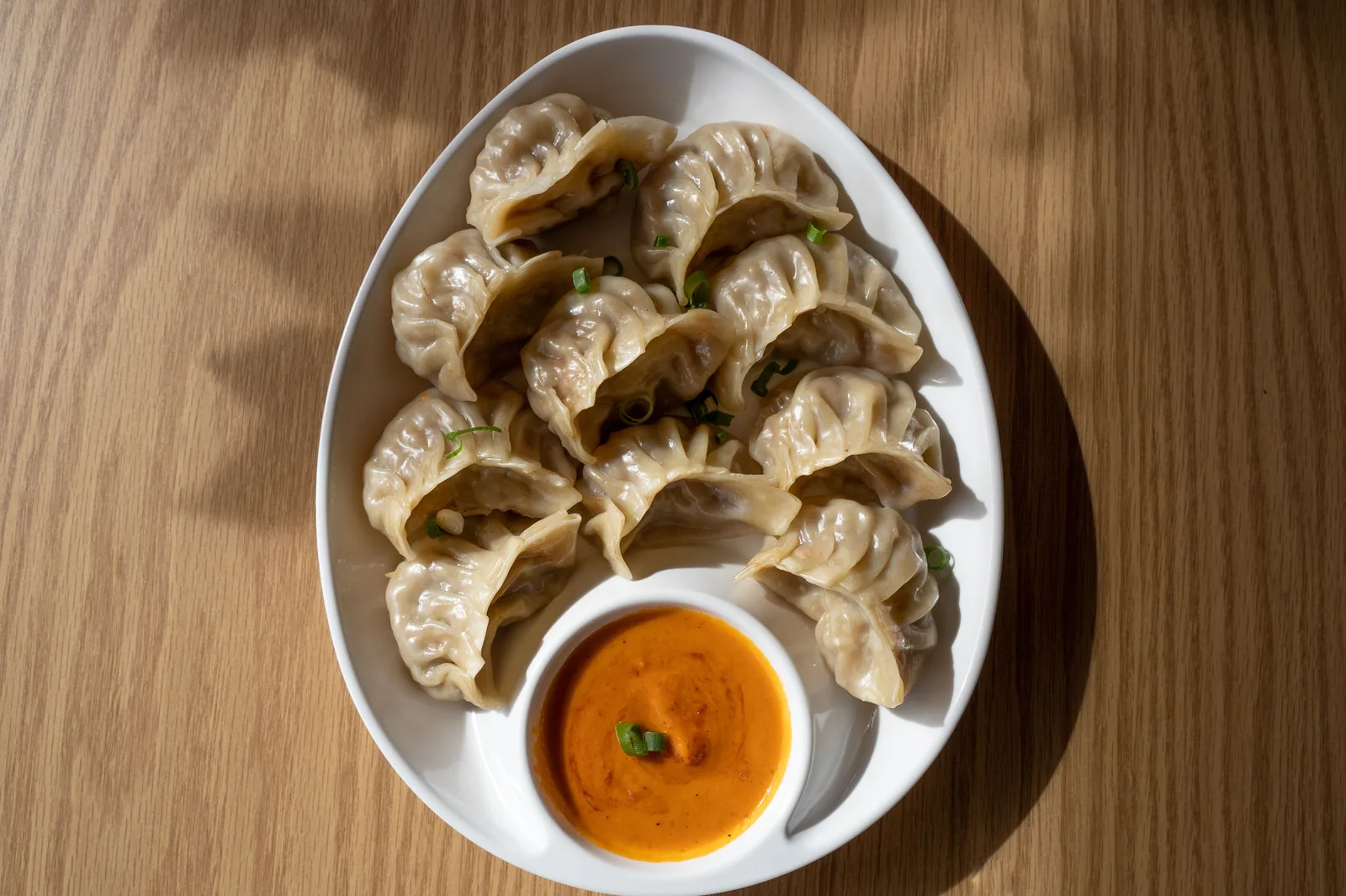 Prato com dumplings dourados e crocantes servidos com molho, em mesa de madeira