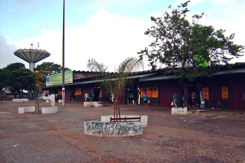 Fileira de bancas da Feira Central de Ceilândia com a caixa d'água ao fundo e placa da feira