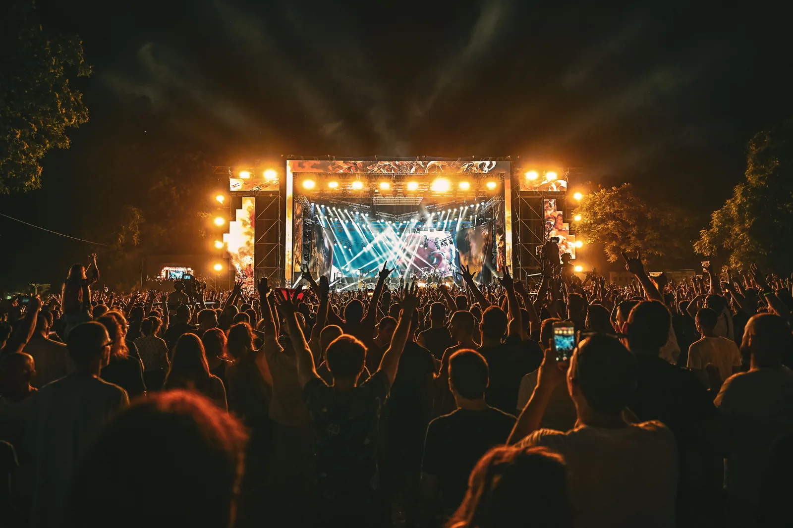 Público de braços erguidos diante de um palco iluminado em festival ao ar livre à noite