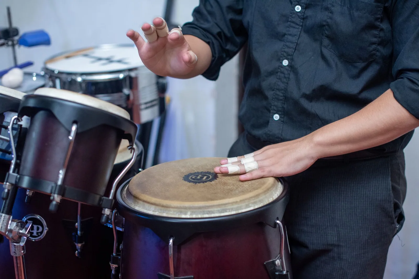 Mãos de músico sobre um conga, ao lado de bongôs, em foto de perto