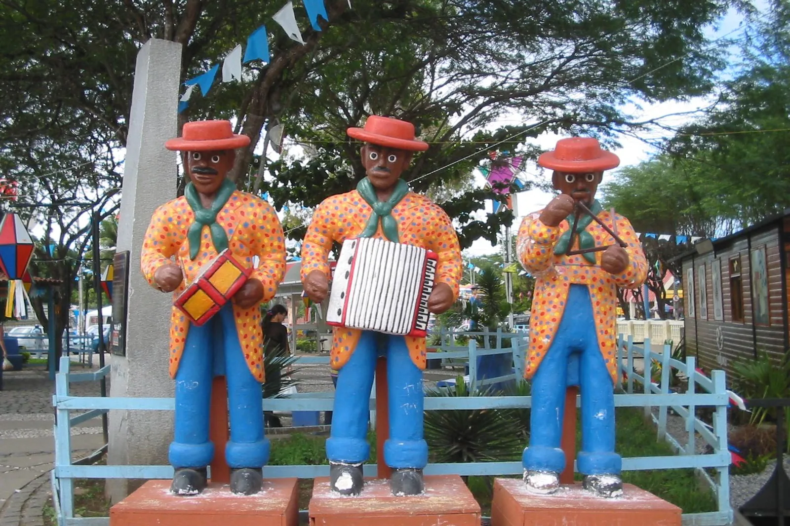 Três estátuas coloridas de músicos de forró, com zabumba, sanfona e triângulo, numa praça de Caruaru, em Pernambuco