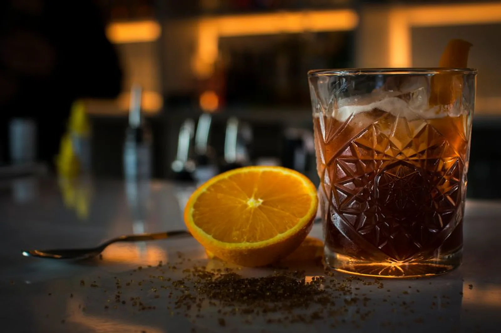 Copo de drink com gelo e meia laranja sobre balcão de bar iluminado