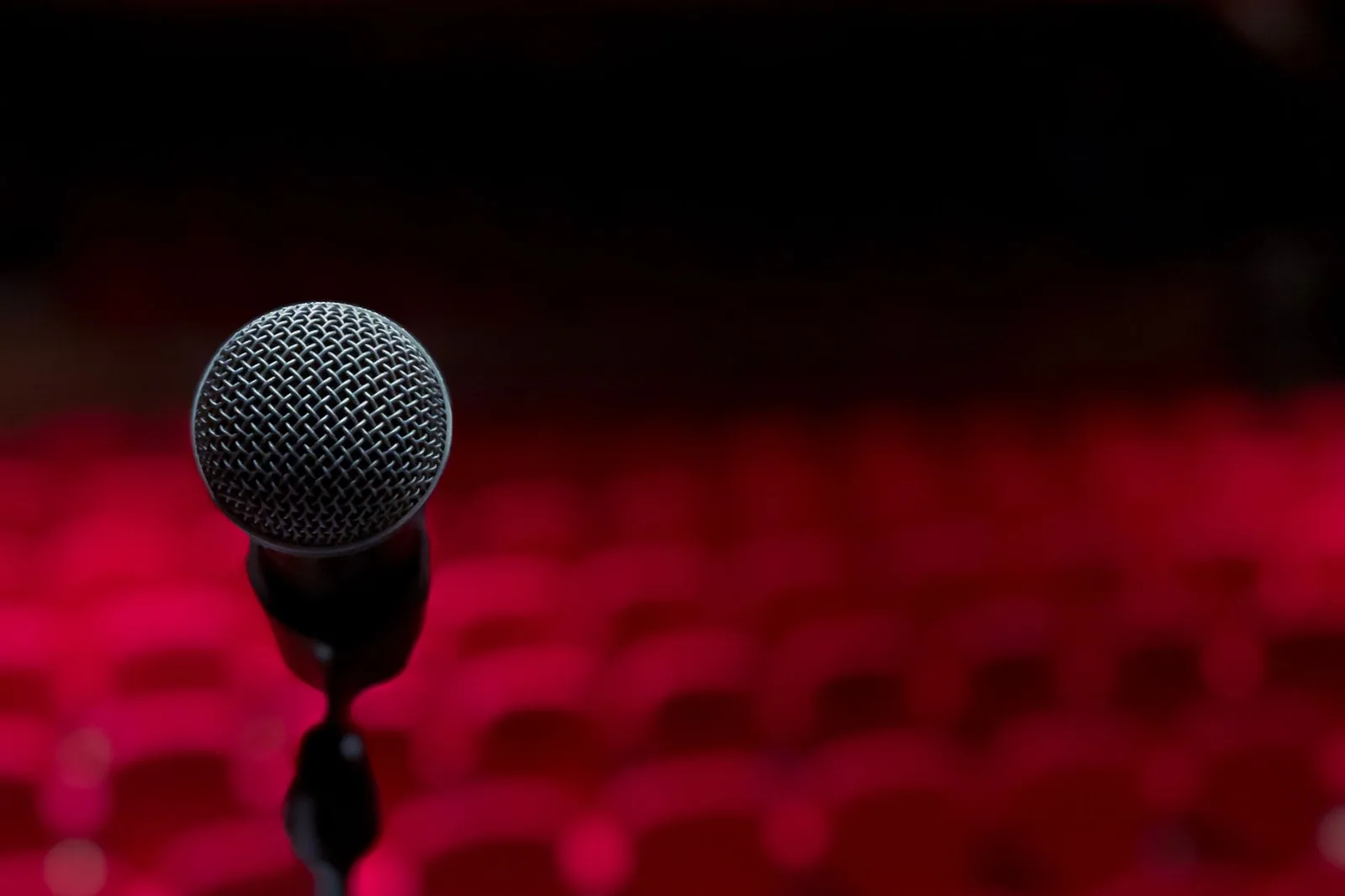 Microfone em close no palco de um teatro, com poltronas vermelhas desfocadas ao fundo (foto de banco de imagens, não é do espetáculo)