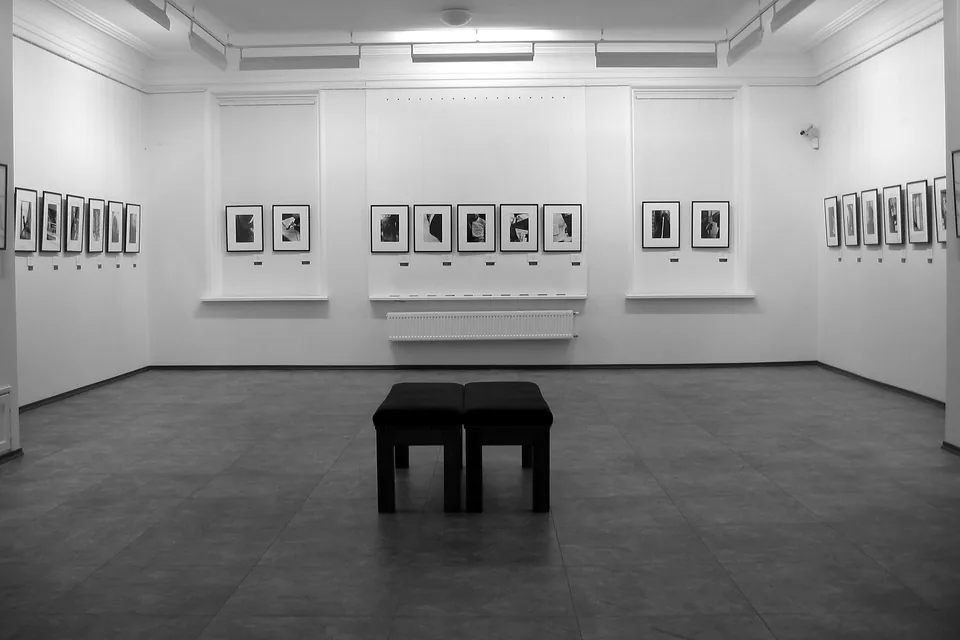 Sala de exposição de paredes brancas com obras emolduradas alinhadas e banco no centro